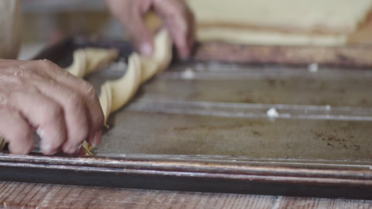 A baker places twisted dough pieces onto a baking sheet, preparing them for baking.