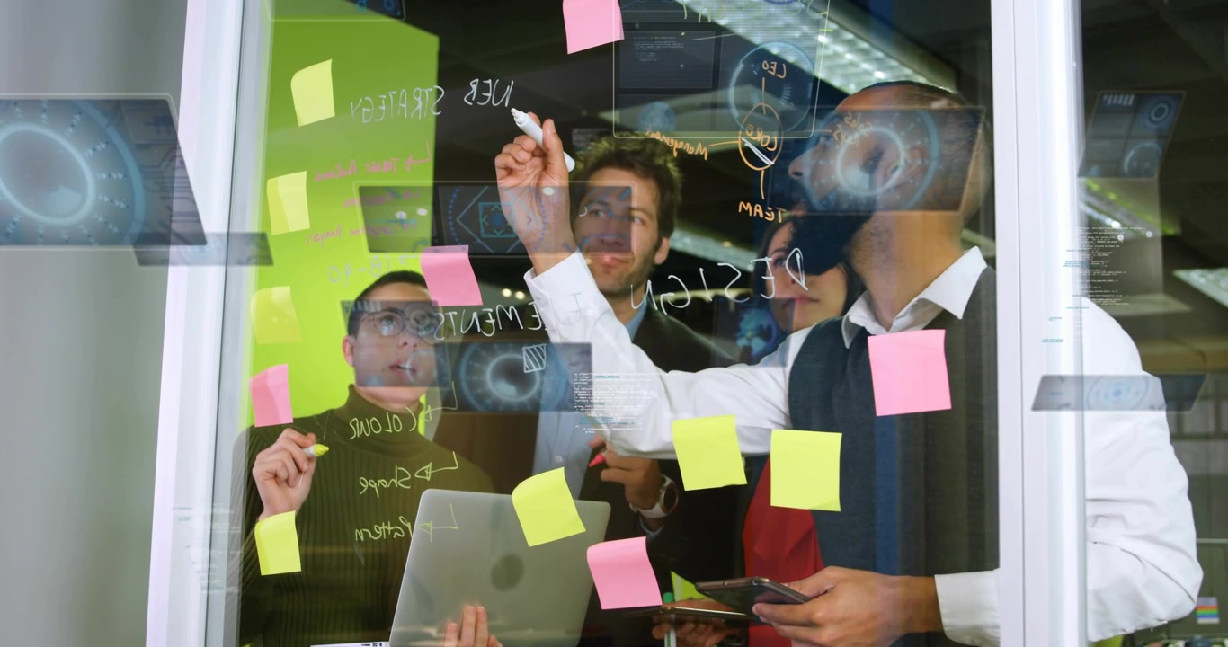 Younger coworker picking marker and writing header on glass partition during business planning