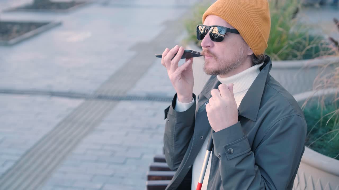 도시 공원 의 벤치 에 앉아 스마트폰 을 들고 있는 눈먼 젊은이 가 전화 하고 있다