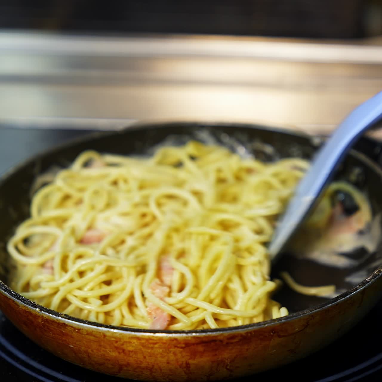 Man`s hands with kitchen spatula mixes pasta with sauce in frying pan. Selective focus. Tasty dinner