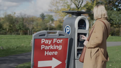 A-woman-pays-for-parking-a-car,-uses-a-solar-powered-parking-meter.