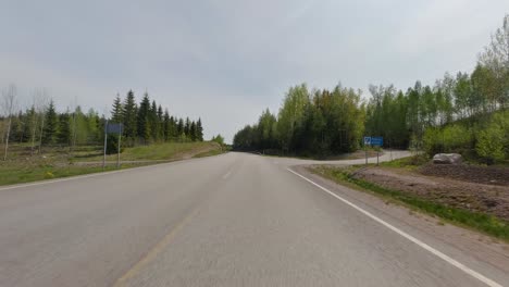 The-car-gracefully-glides-along-the-road,-traversing-through-the-enchanting-landscape-of-the-forest-and-the-expansive-green-fields