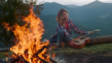 un músico atractivo viaja por las montañas. una mujer joven disfruta de la quema de una fogata de cerca