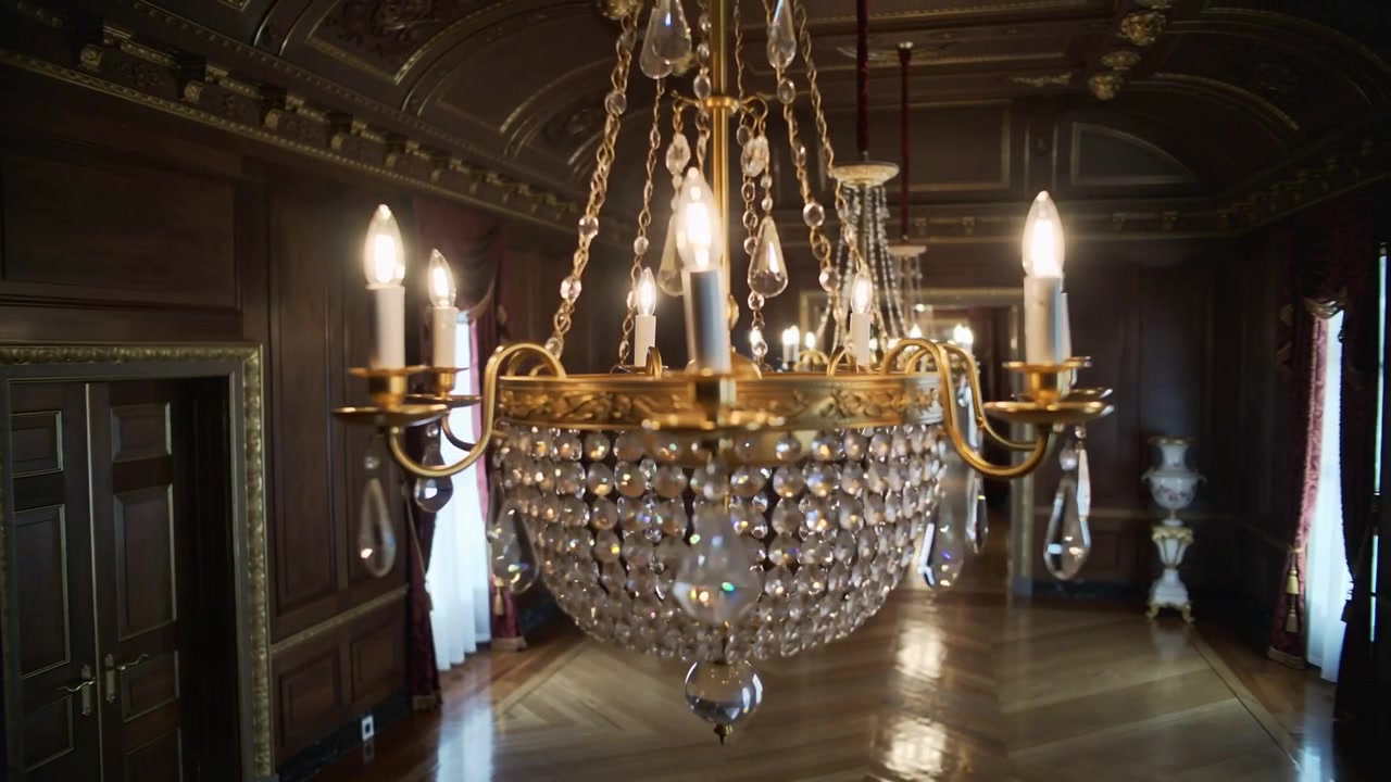 La telecamera si muove in panoramica, rivelando un lampadario dorato che si illumina in una sala formale per evidenziare i dettagli.