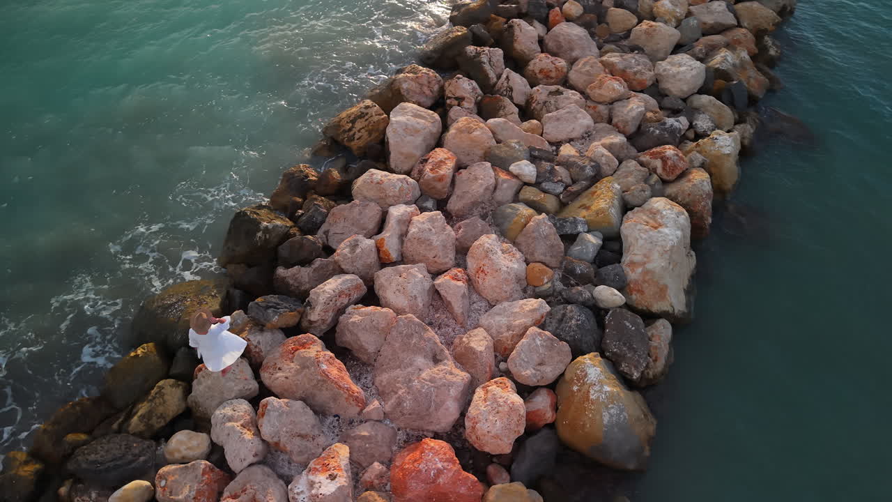 Luftfoto af kvinde, der står på en klippemole ved havet.