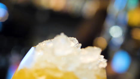 Pouring-yellow-soda-into-glass-with-ice-in-slow-motion,-fizzling-closeup