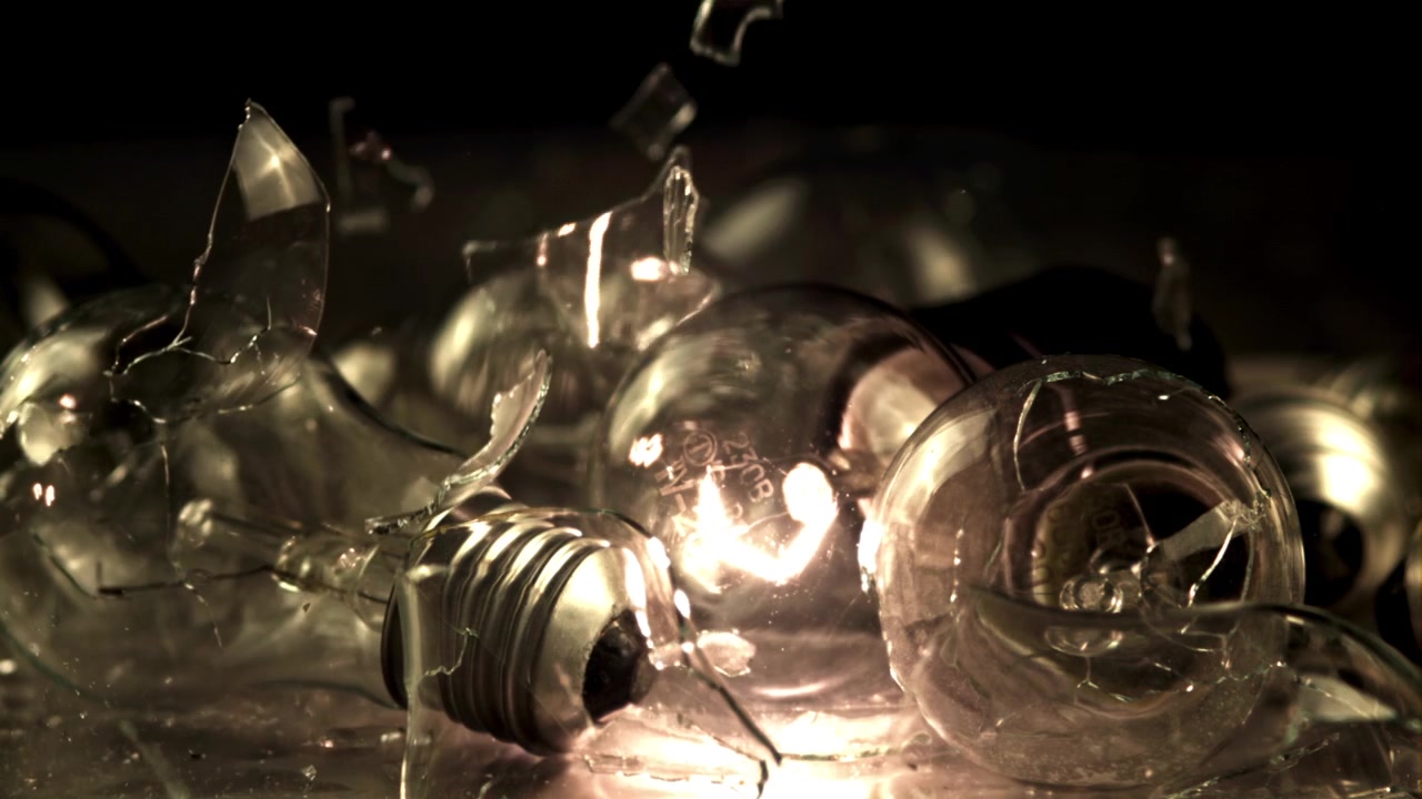 Broken Light Bulbs with Glowing Filament and Falling Glass Shards in Slow Motion