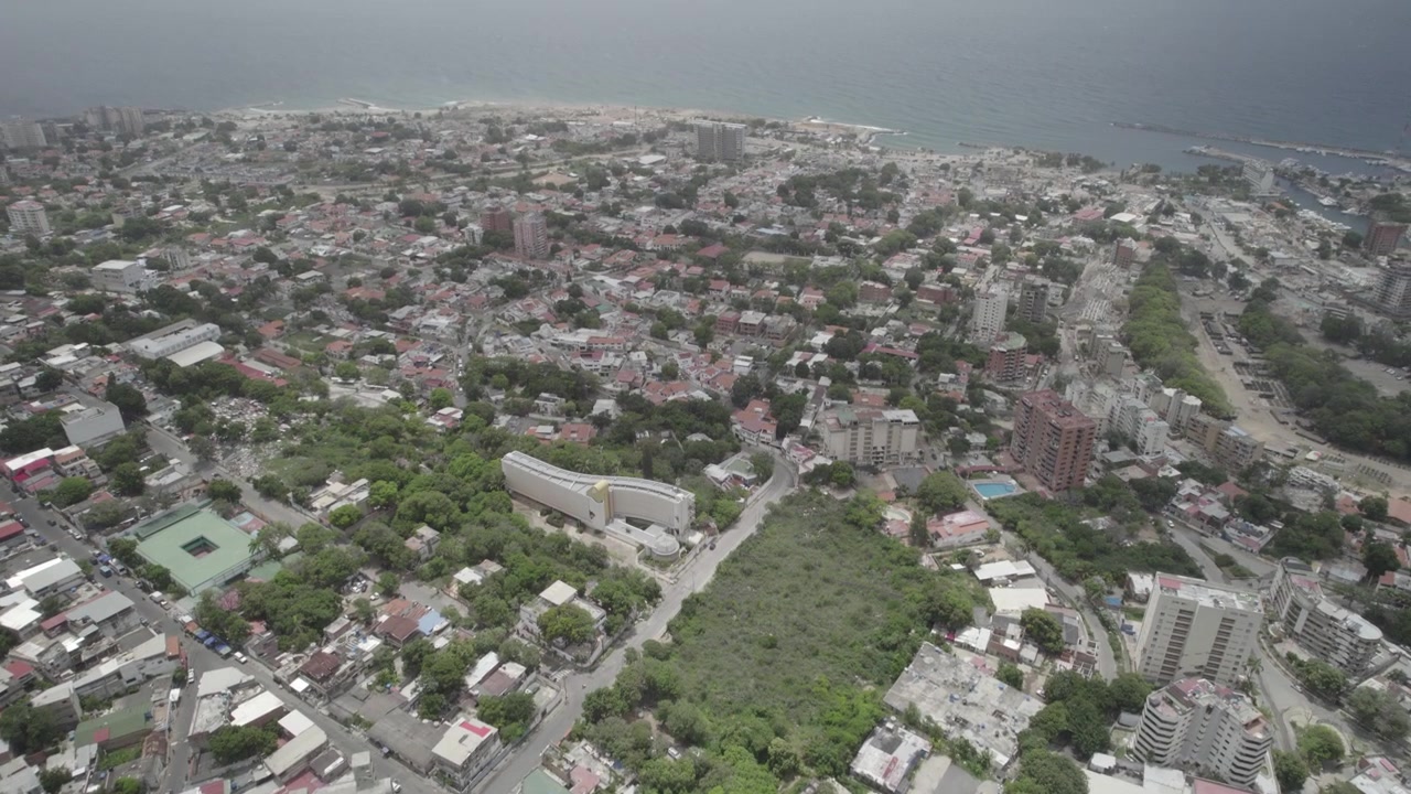 Griglia urbana densa di Caraballeda, ripresa dall'alto, con case ravvicinate, strade locali e aree di alberi verdi, che si trasforma in una ripresa in tilt-up che rivela il Mar dei Caraibi e un campo da golf. 4k Dlog