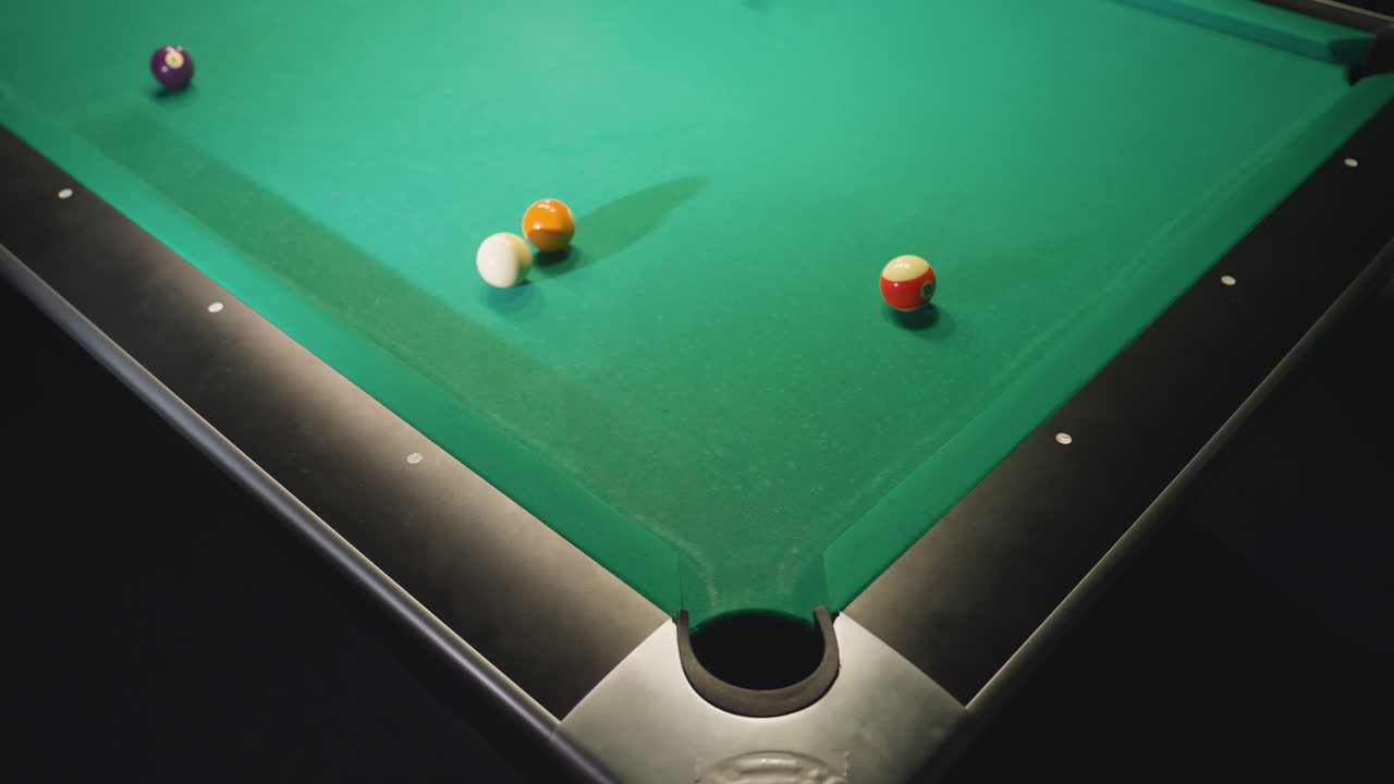 Up view of white billiard ball rolling across green pool table after striking green ball and sinking into pocket. Motion blur captures speed, precision, and intensity of gameplay