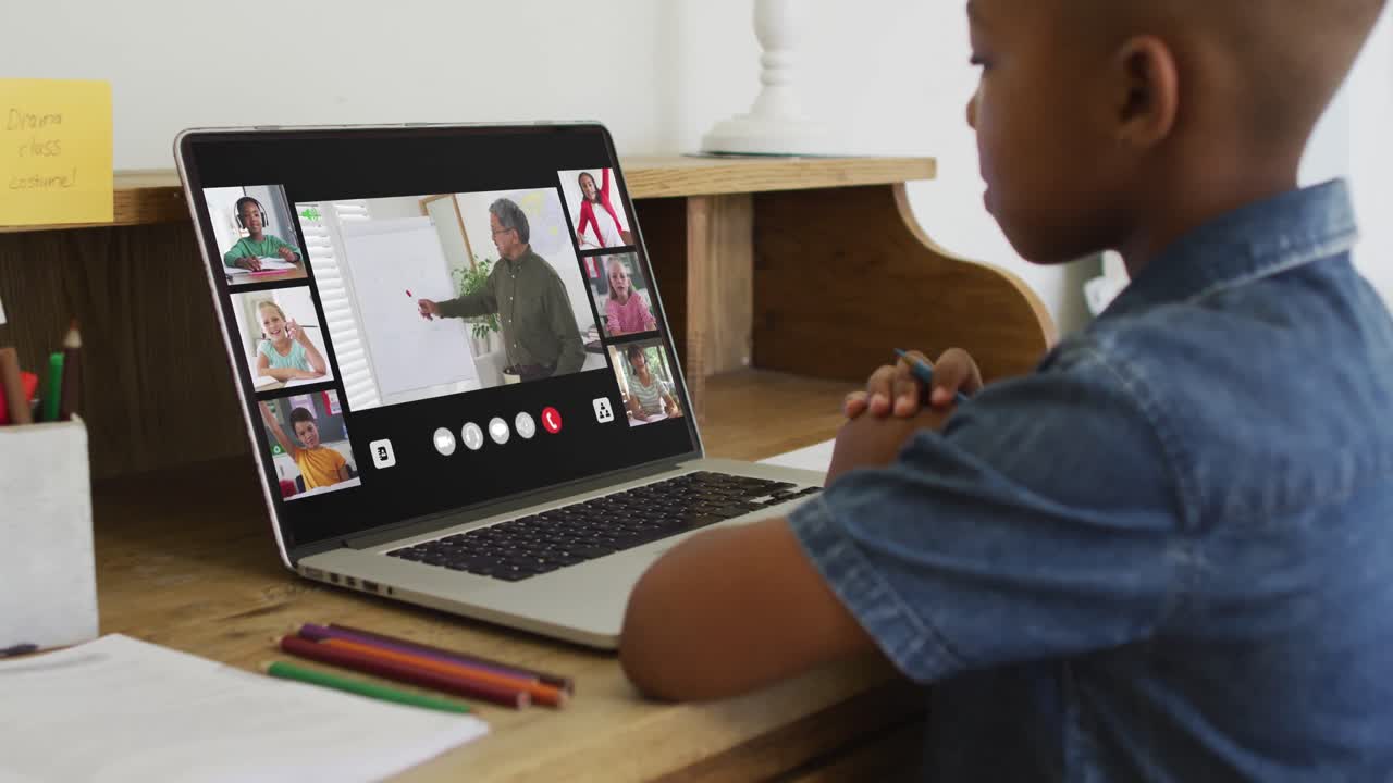 African american boy holding a pencil having a video conference on laptop at home