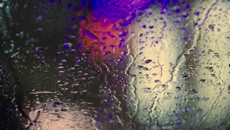 close up of rain water drops on car window glass with blurred traffic lights background at night.