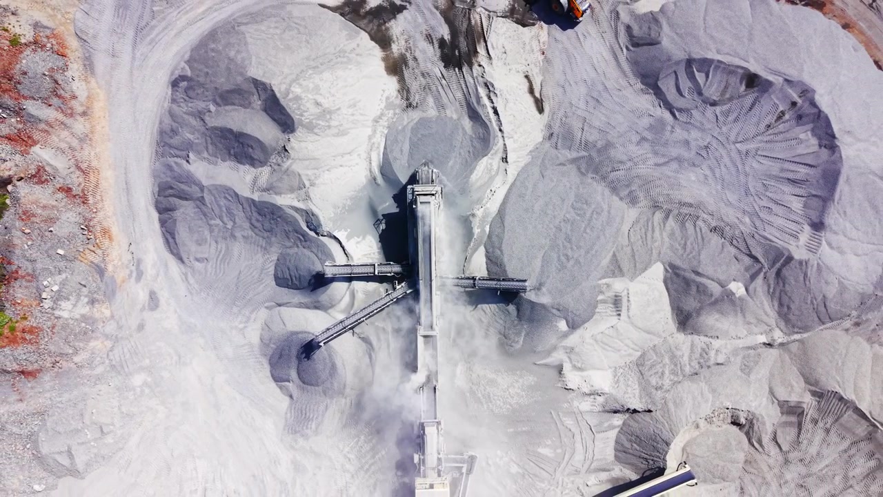 Drone perspective of mechanical sorting machinery shifting aggregate between grey material piles. Abstract top down view of industrial conveyor belt system