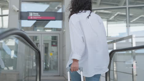 woman with luggage on escalator at airport