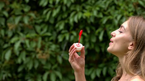 una mujer que sopla burbujas contra un fondo de planta de cobertura verde natural