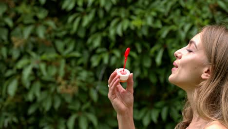 a woman blowing bubbles against a background of natural green hedge plant