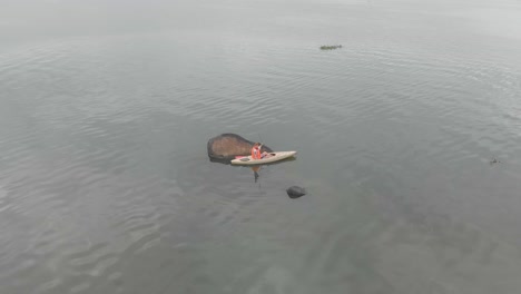 aerial orbiting around a man fishing from a kayak on lake victoria near a granite bolder