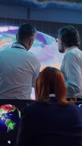 zoom in view of woman leaving workplace while men examining earth scheme on large screen and discussing global warming during work in ecology control center