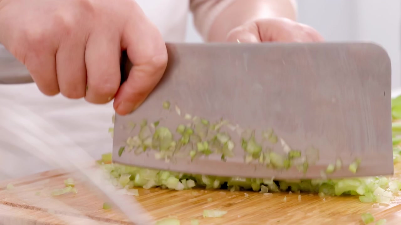 Mani non identificate di una donna chef che trita erba cipollina fresca o taglia cipollotti verdi su un tagliere da cucina con un coltello per preparare gustosi fagottini fatti in casa ripieni di carne macinata e verdure