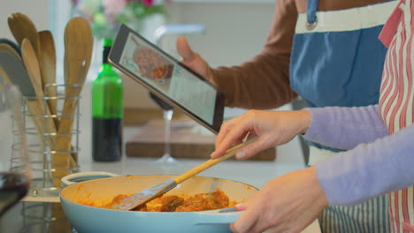 mature couple at home following recipe on digital tablet in kitchen as they prepare meal together - shot in slow motion