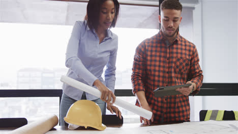 Diverse-male-and-female-architects-with-tablet-discussing-blueprints-standing-in-office,-slow-motion