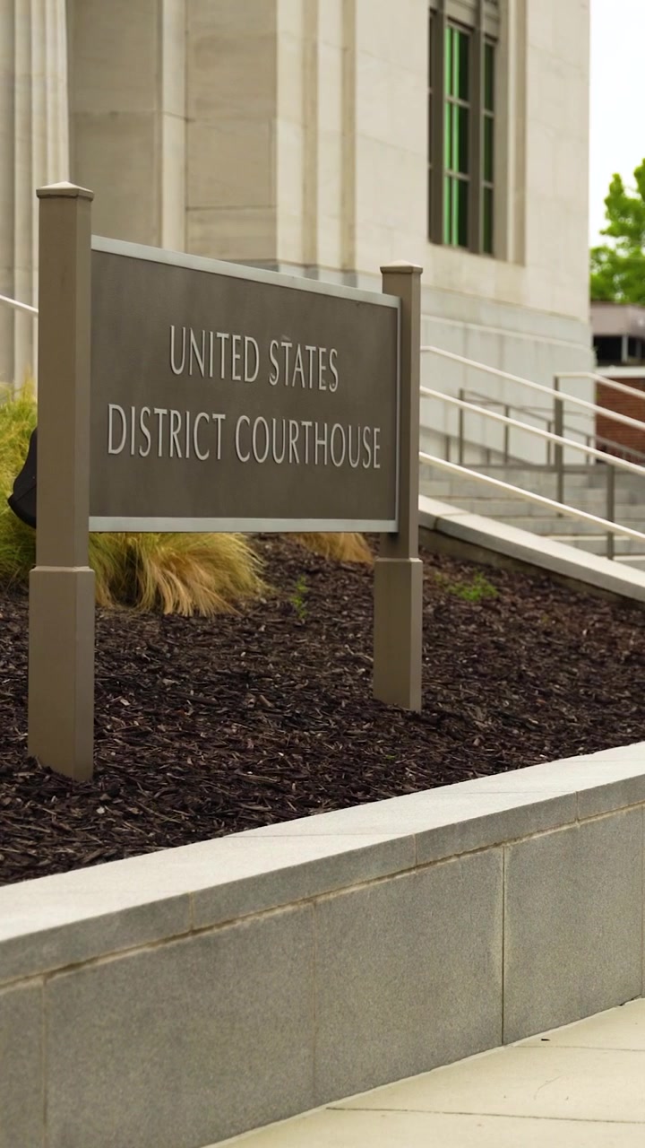 Uno scatto verticale cattura il tribunale distrettuale degli Stati Uniti nel centro di Mobile, Alabama, caratterizzato da alte colonne, segnaletica del tribunale, scale, verde paesaggistico e un maestoso design civico.