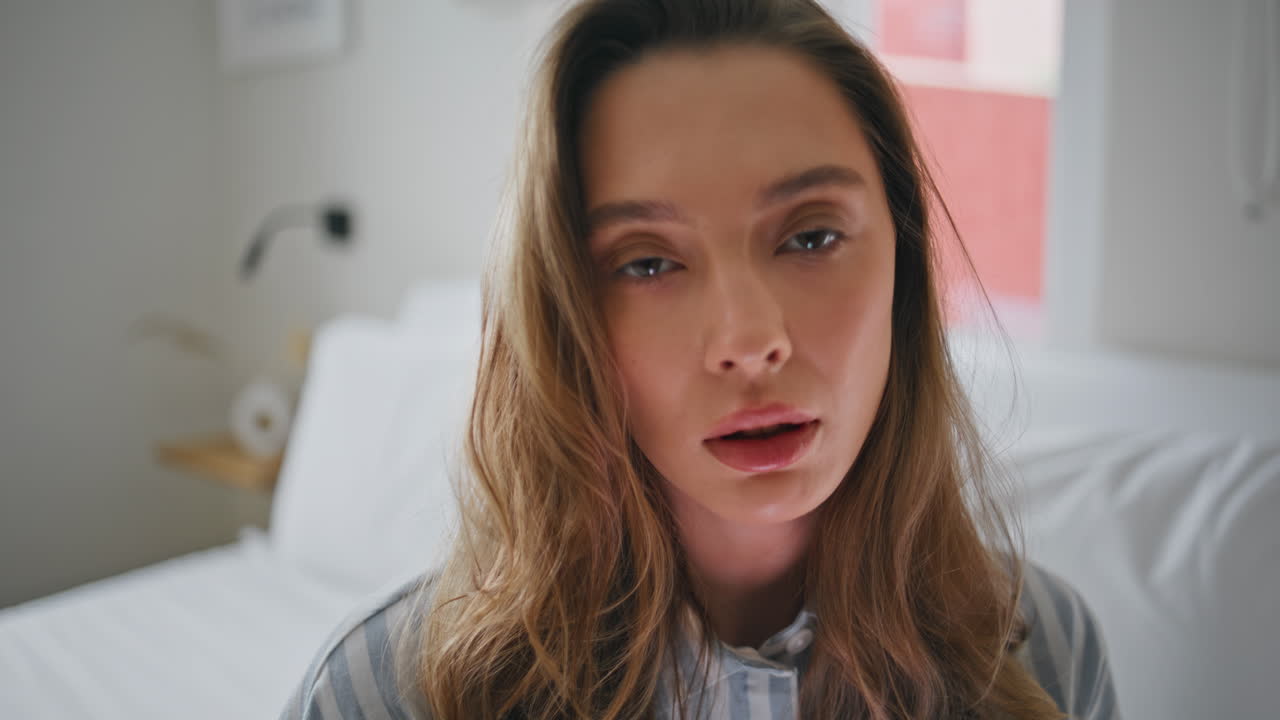 Portrait sad woman bedroom looking camera with serious gaze. Lady sitting bed