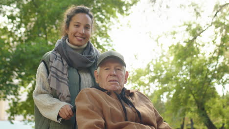 portrait of caregiver and elderly man in wheelchair in park