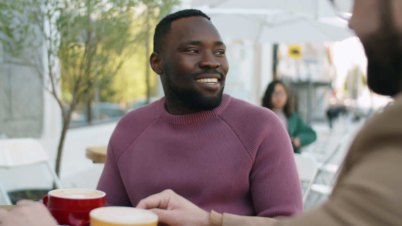Cheerful African American Man Chatting with Colleague over Coffee in Outdoor Cafe
