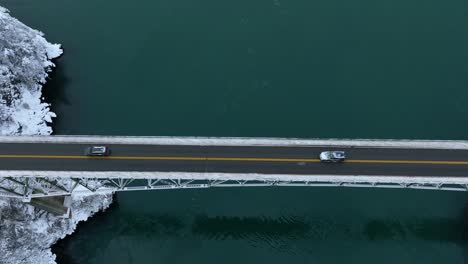 top down aerial view of cars driving across deception pass state park in the snow