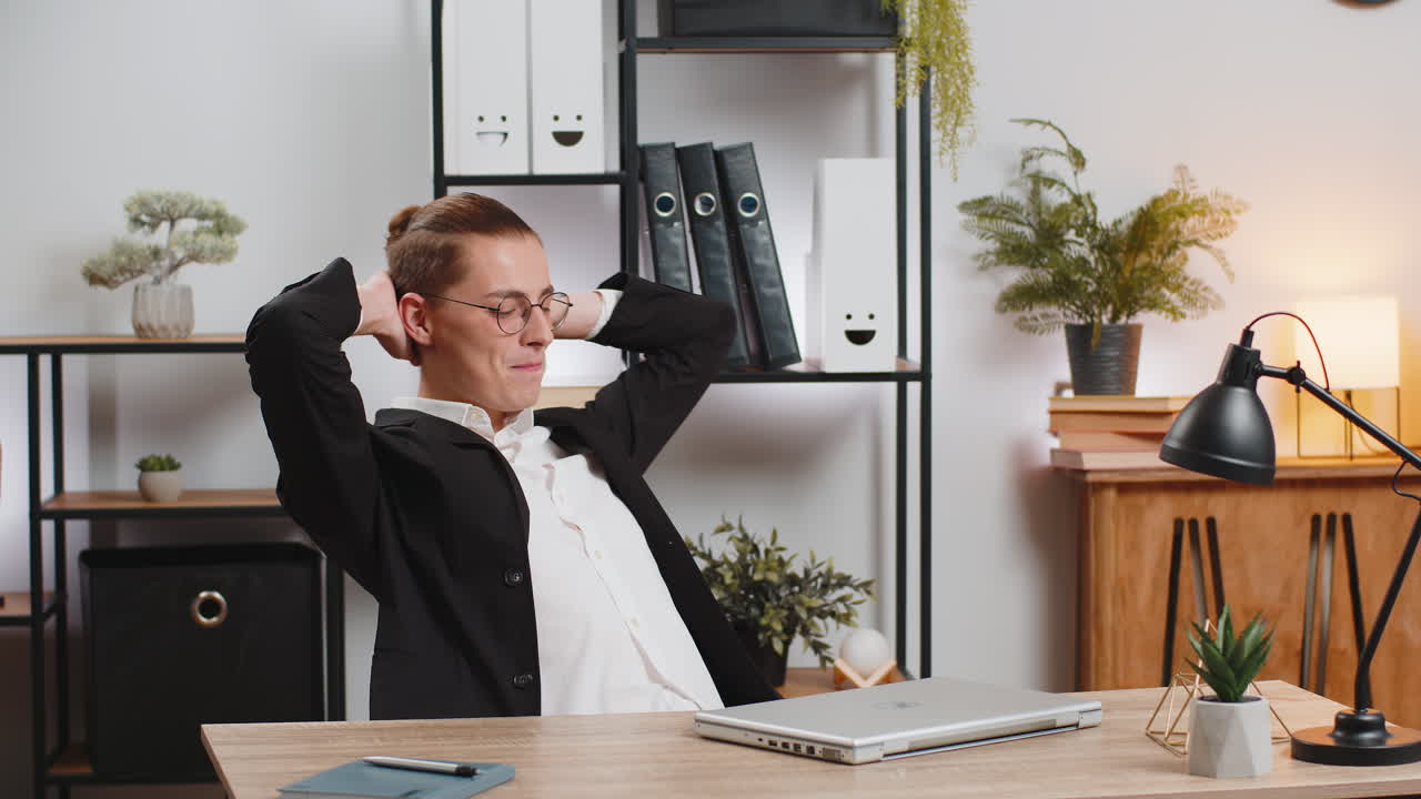 Smiling young businessman closing laptop after finishing work and taking break at home office table