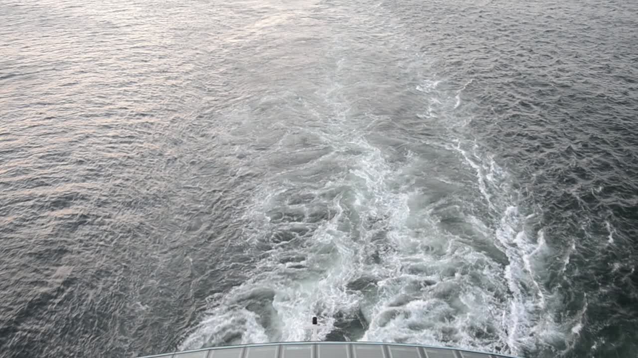 The stern of a cruise ship which is cutting through the ocean leaving icy blue waves in its way