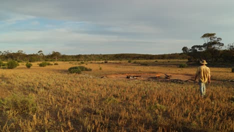 an australian bushman walks to his camp in an open field in the outback