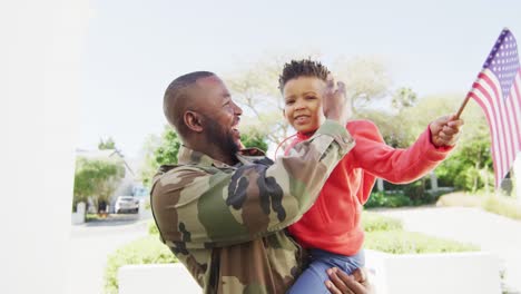 happy african american father with son embracing and waving flag of usa