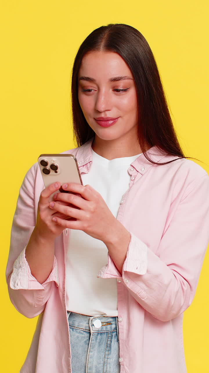 Donna che digita messaggio sullo smartphone, sorridendo timidamente, mordendosi il labbro, espressione emotiva romantica, innamoramento.