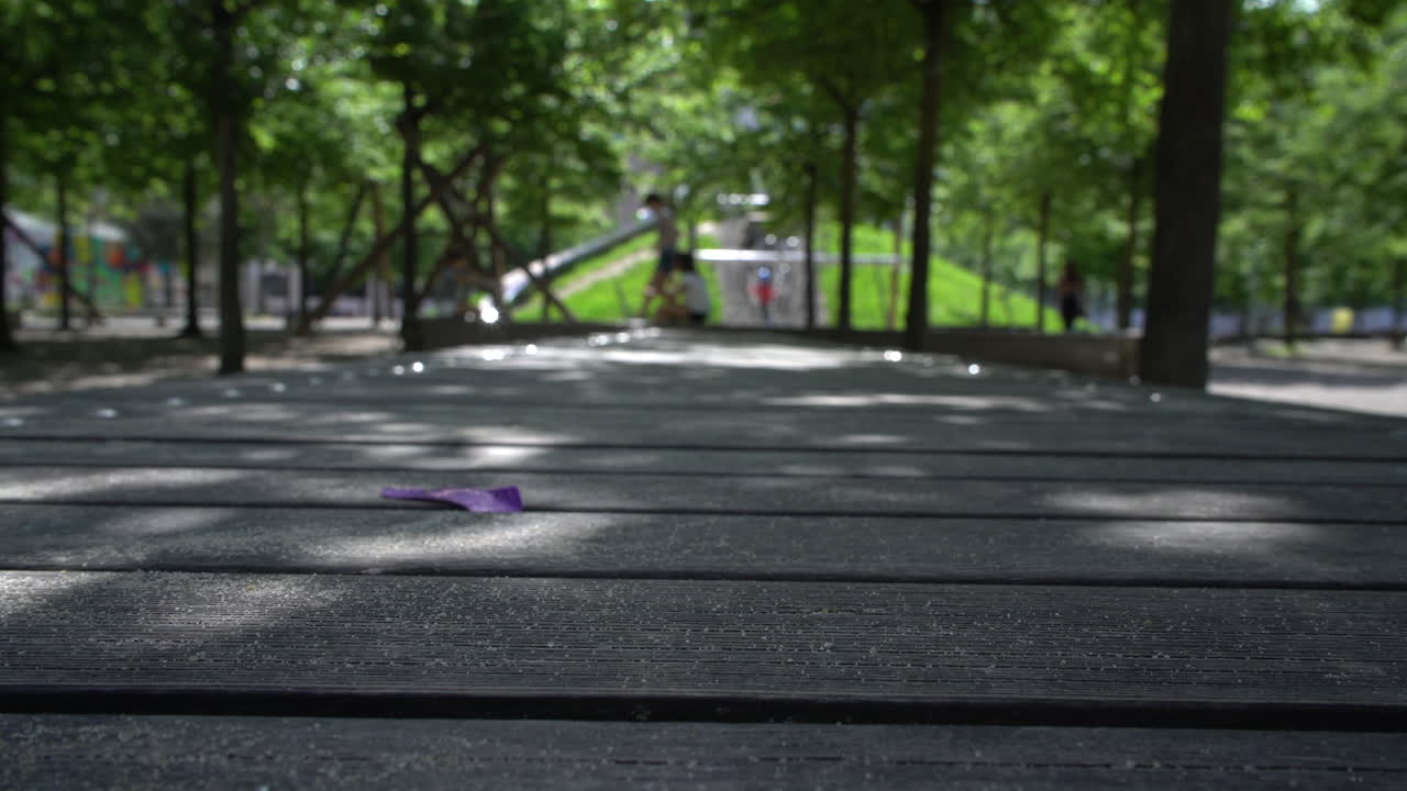 Children playing on a playground in the city, in the shade of the trees, on a false ship, the children are blurred, in the foreground a sharp bench with the beautiful shadows of leaves