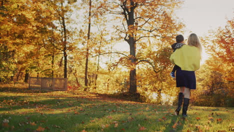 Mom-carries-a-baby-in-her-arms,-walks-through-a-beautiful-park-at-sunset