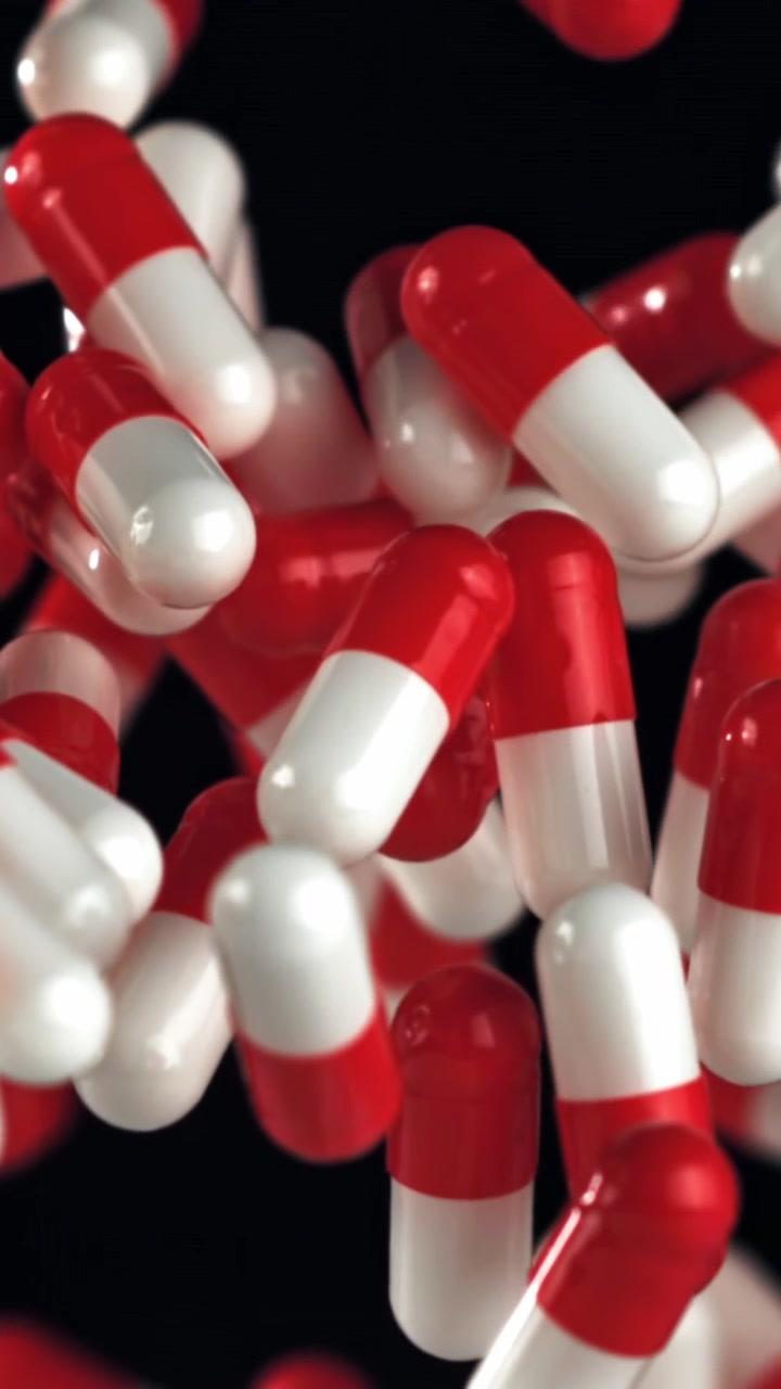 Red and White Medical Capsules Falling in Slow Motion Against a Black Background