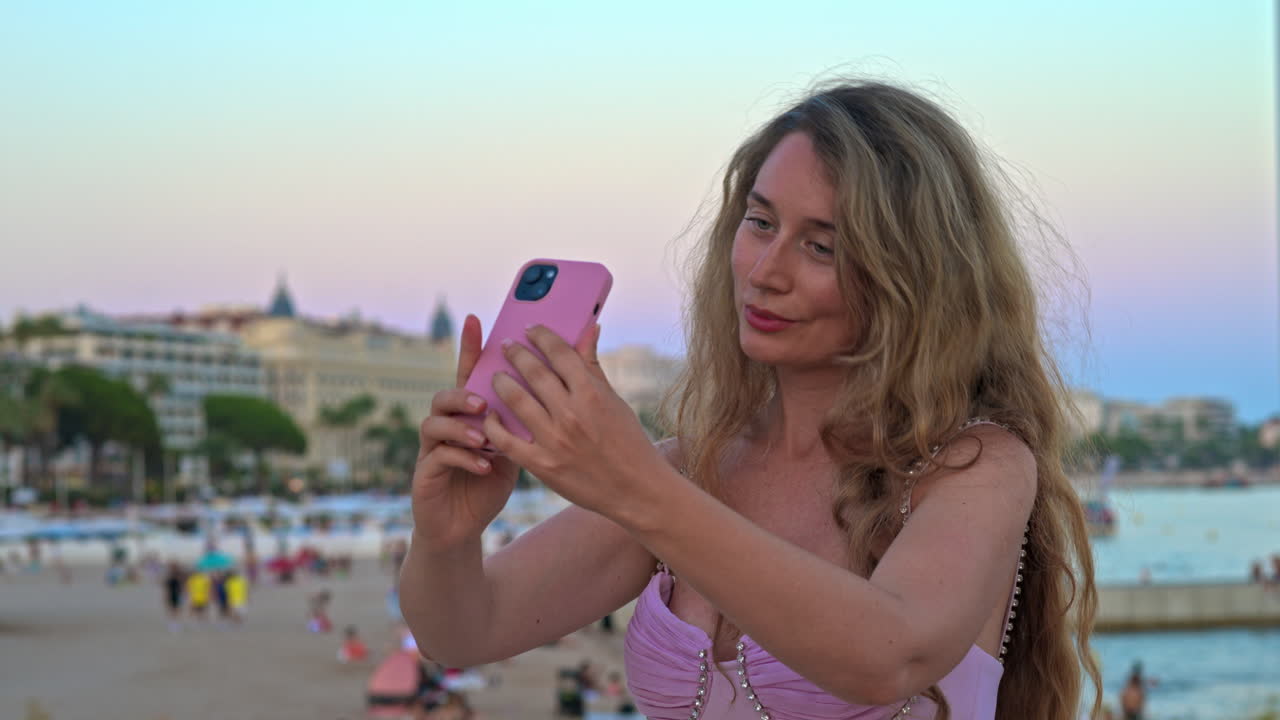 Woman in pink dress taking pictures at the beach in the evening in Cannes, France