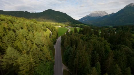 fpv drone flying fast above an empty alpine road in the mountains surrounded by a forest pine trees in the region of tyrol, austrian alps