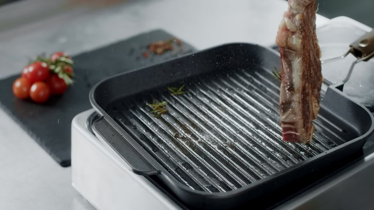 Chef preparing meat at griddle. Closeup chef hands turning steak with tongs.