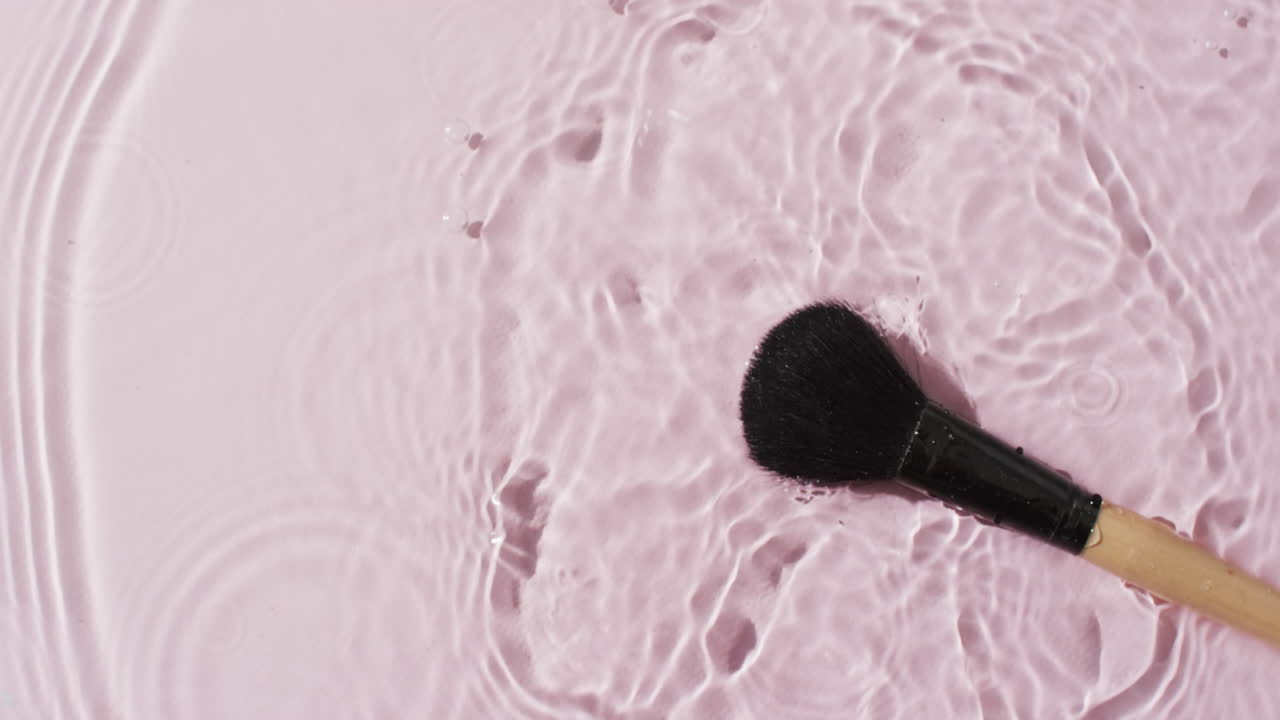 Video of make up brush in water with copy space on pink background