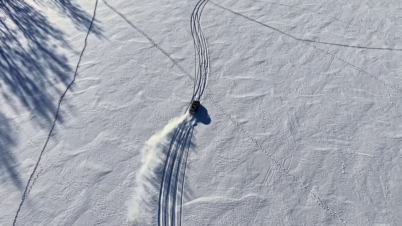 Ripresa aerea dall'alto di un'auto che derapa e crea tracce su un terreno aperto innevato.