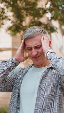 displeased man rubbing temples to cure headache problem suffering from migraine stress on street