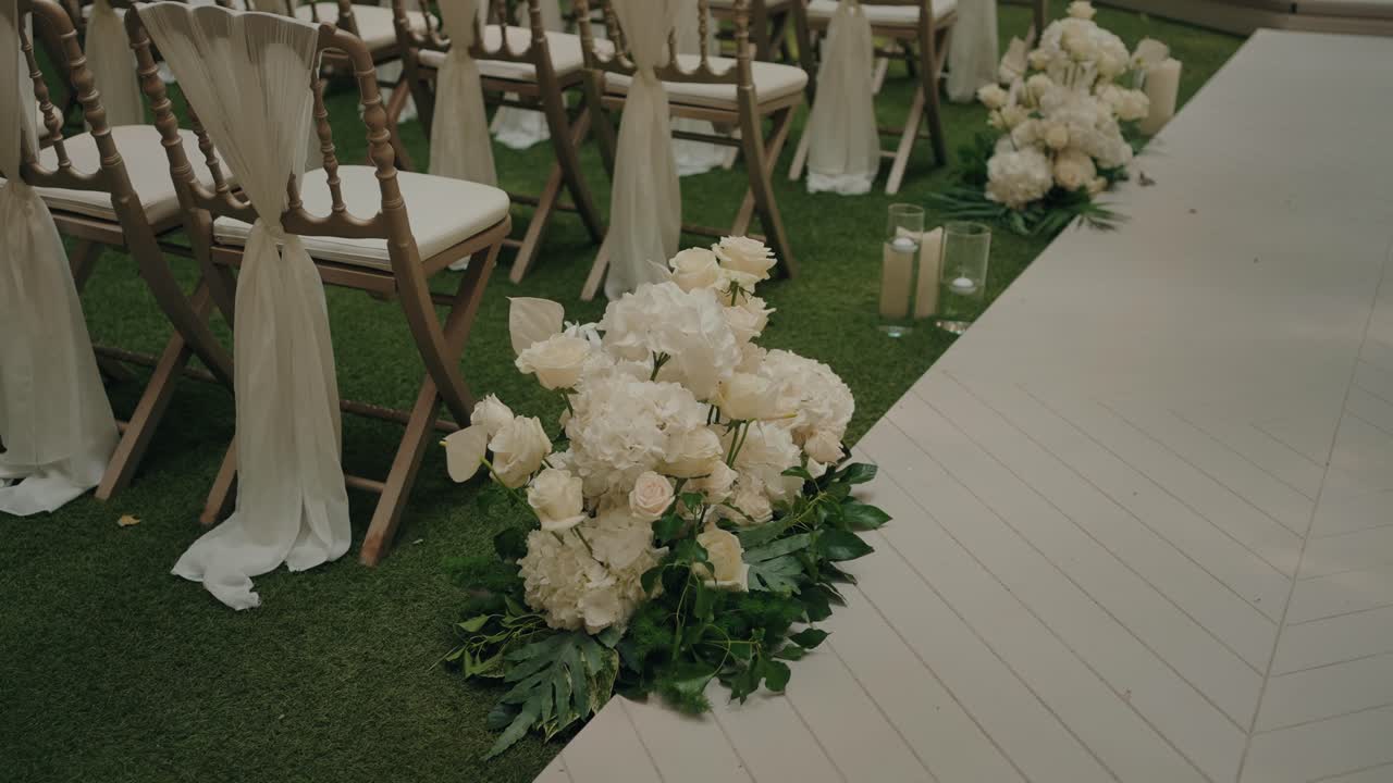 Fiori bianchi e candele decorano le sedie lungo il corridoio di una cerimonia nuziale.
