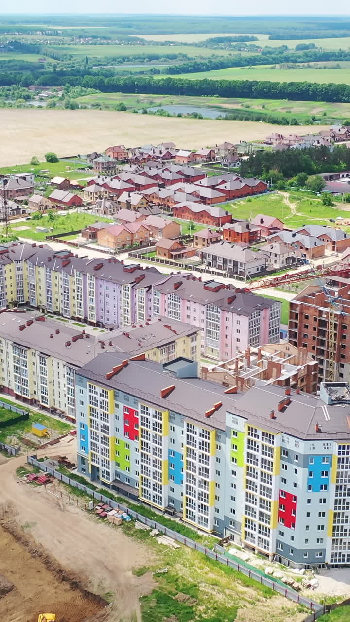 Modern residential complex in the countryside. Colorful high-rise buildings on a construction site. New microdistrict is building. Aerial view. Vertical video