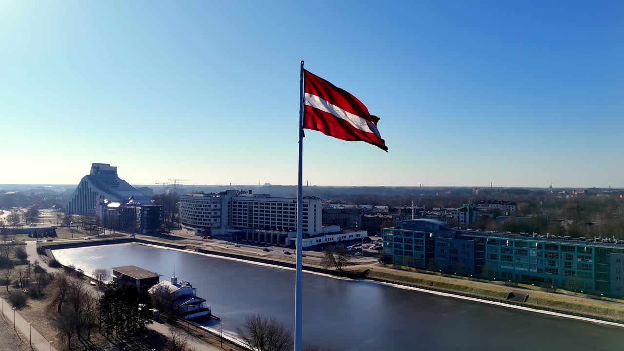 una bandera roja y blanca de letonia está volando alto sobre una ciudad riga