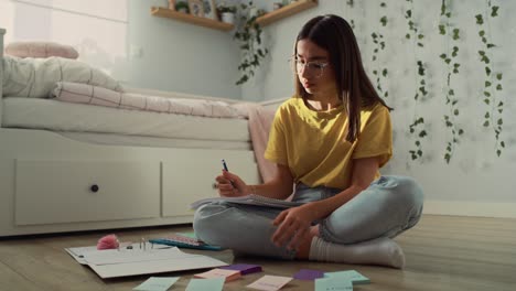 adolescente caucásica sentada en el suelo y aprendiendo de tarjetas flash y cuaderno