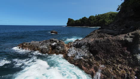 Low-FPV-drone-flyover-over-ocean-waves-crashing-against-rocky-Hawaiian-coast