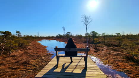 a lady sitting on a timber bench seat on a wooden platform in wilderness setting