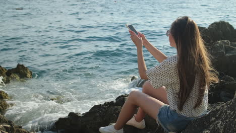 woman taking photo of ocean waves from rocks by the coast